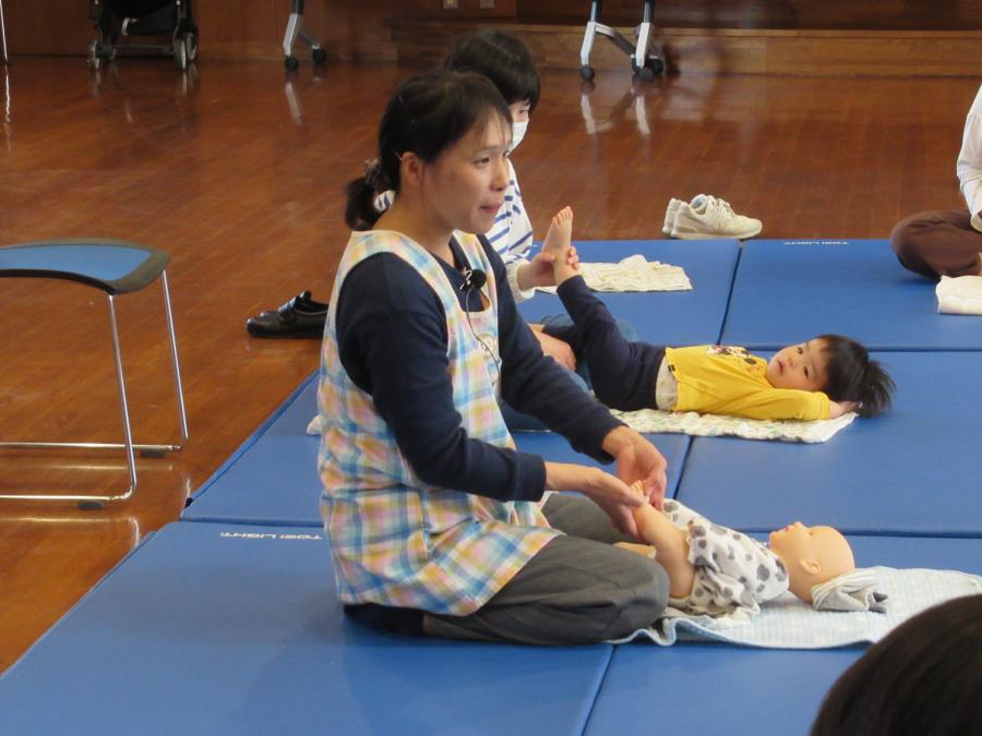 講師が人形の赤ちゃんを下に寝かせてマッサージの仕方を教える様子