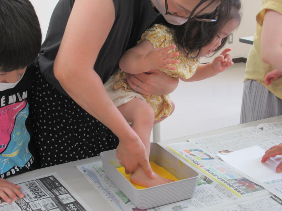 お母さんが抱っこして子どもの足型を取るために片足をスタンプ台に入れ、絵の具をつけている様子