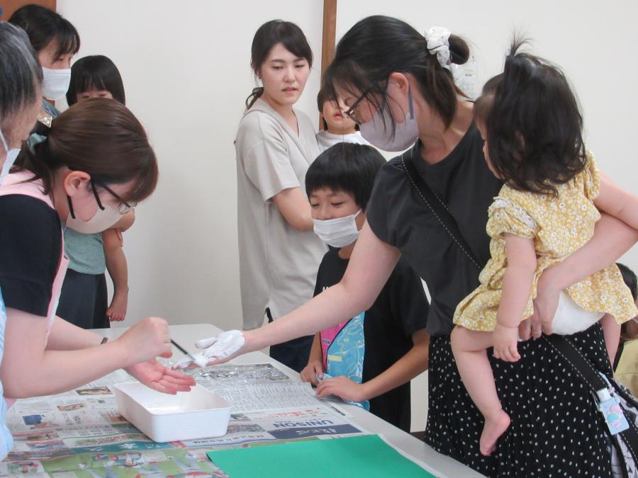 お母さんが子どもを抱っこしながら、右手に絵の具をつけてもらっているところ