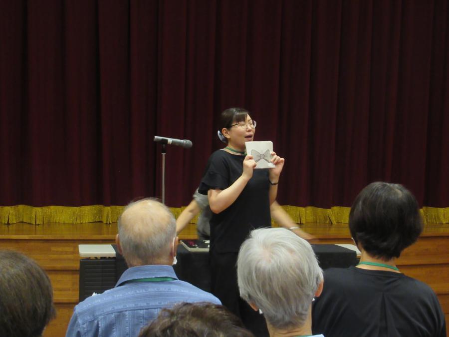 折りたたんで蝶ネクタイになっている紙を持って演じる講師の様子