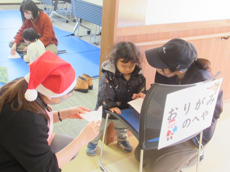 廊下の椅子の上で折り紙を折る一組の親子の写真