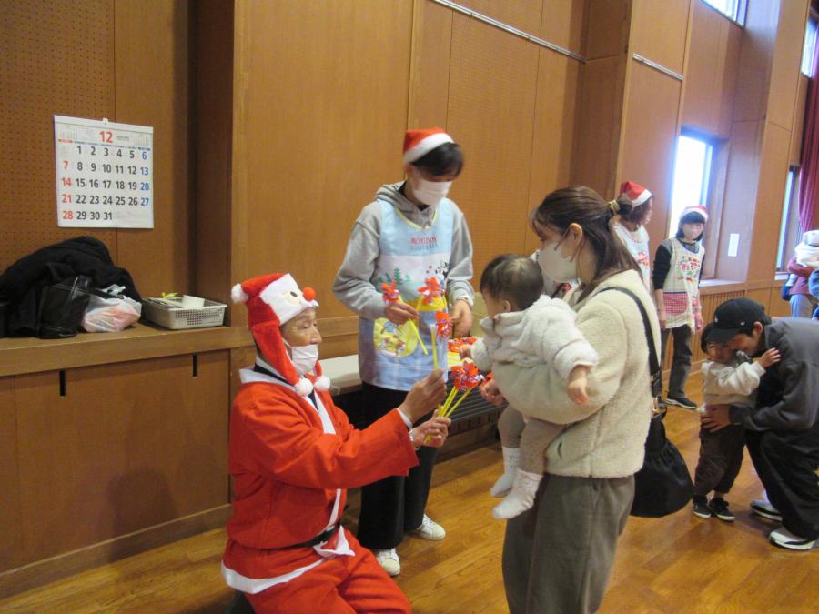 抱っこしたお母さんと子どもがサンタ館長から風車を受け取る様子