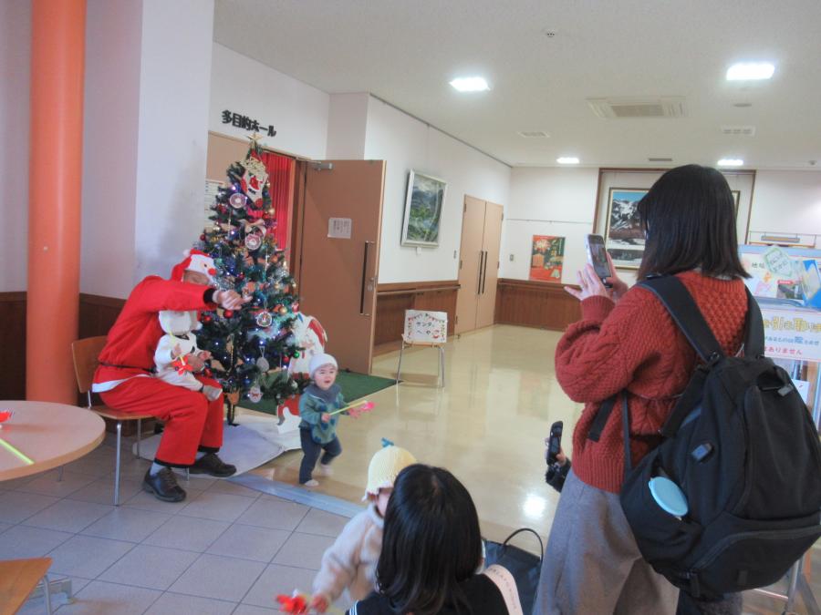 クリスマスツリーの前でサンタ館長と一緒に写真を撮る親子の様子