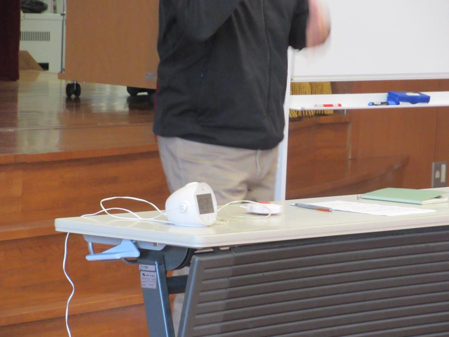 聴覚障害者用のいろいろな機械を机の上に並べて見せている様子