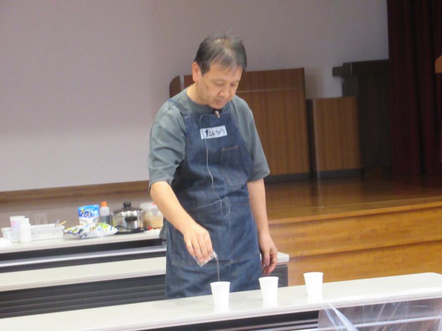 講師が3個の紙コップを並べて水を入れ、実験をしている様子